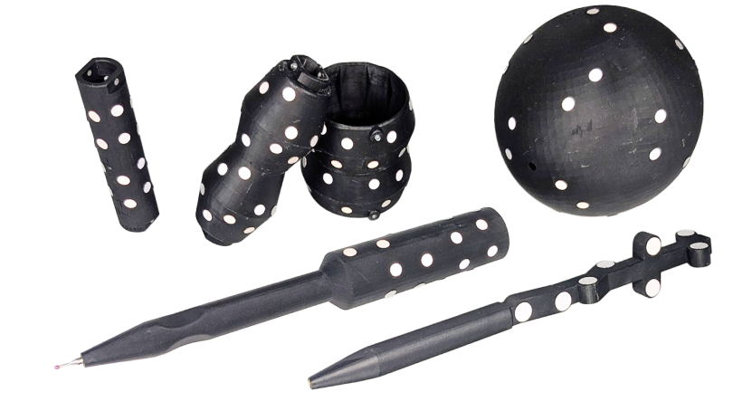 A set of black objects with white polka dots, including a ball, two pens, a cross-shaped tool, and two cylindrical and two irregularly shaped containers.