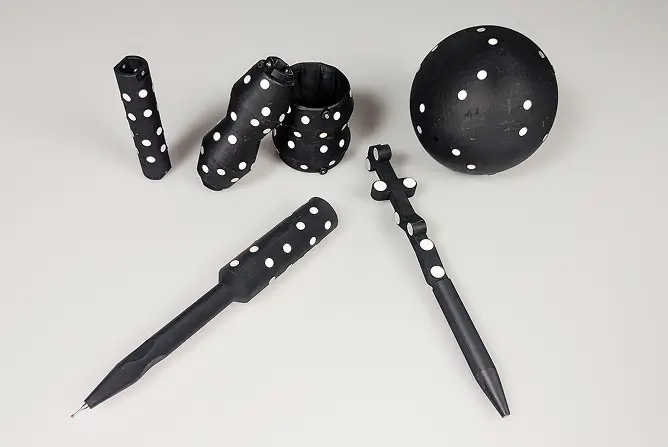 Five black objects with white polka dots, including a sphere, twisted shapes, and two pens, are arranged on a light gray surface.