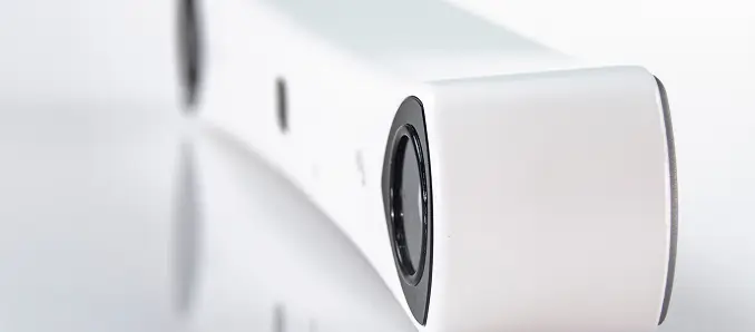 A close-up view of a sleek, modern white electronic device with a rounded edge and a prominent black circular lens or sensor on one end, set against a white background.