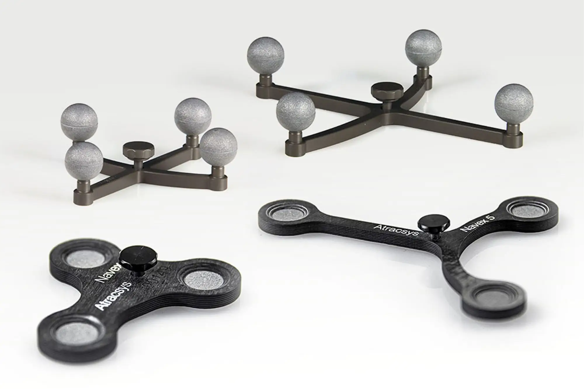 Four black, three-pronged spinner devices are displayed on a light surface; two have metallic spheres on each arm, and two have flat circular ends with labels reading Atracsis and Alexey S.