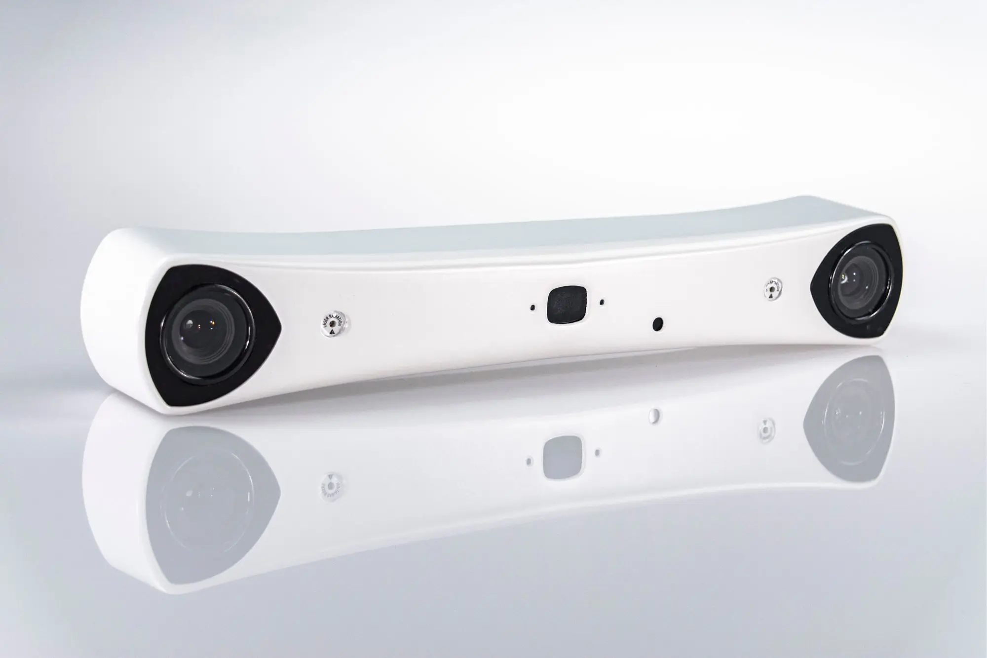 A white, curved electronic device with two large camera lenses on each end and a smaller lens or sensor in the center, placed on a glossy white surface against a light background.