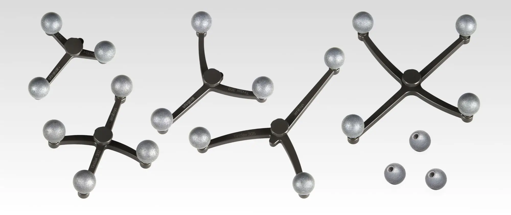 Four black, Y-shaped plastic frames with spherical fiducials—silver balls at the ends—are arranged on a white background. Three loose silver balls are also placed nearby the frames.